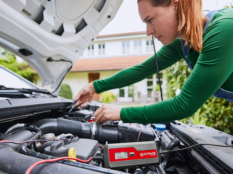 Une femme utilise un chargeur de batterie Ultimate Speed pour sa voiture.