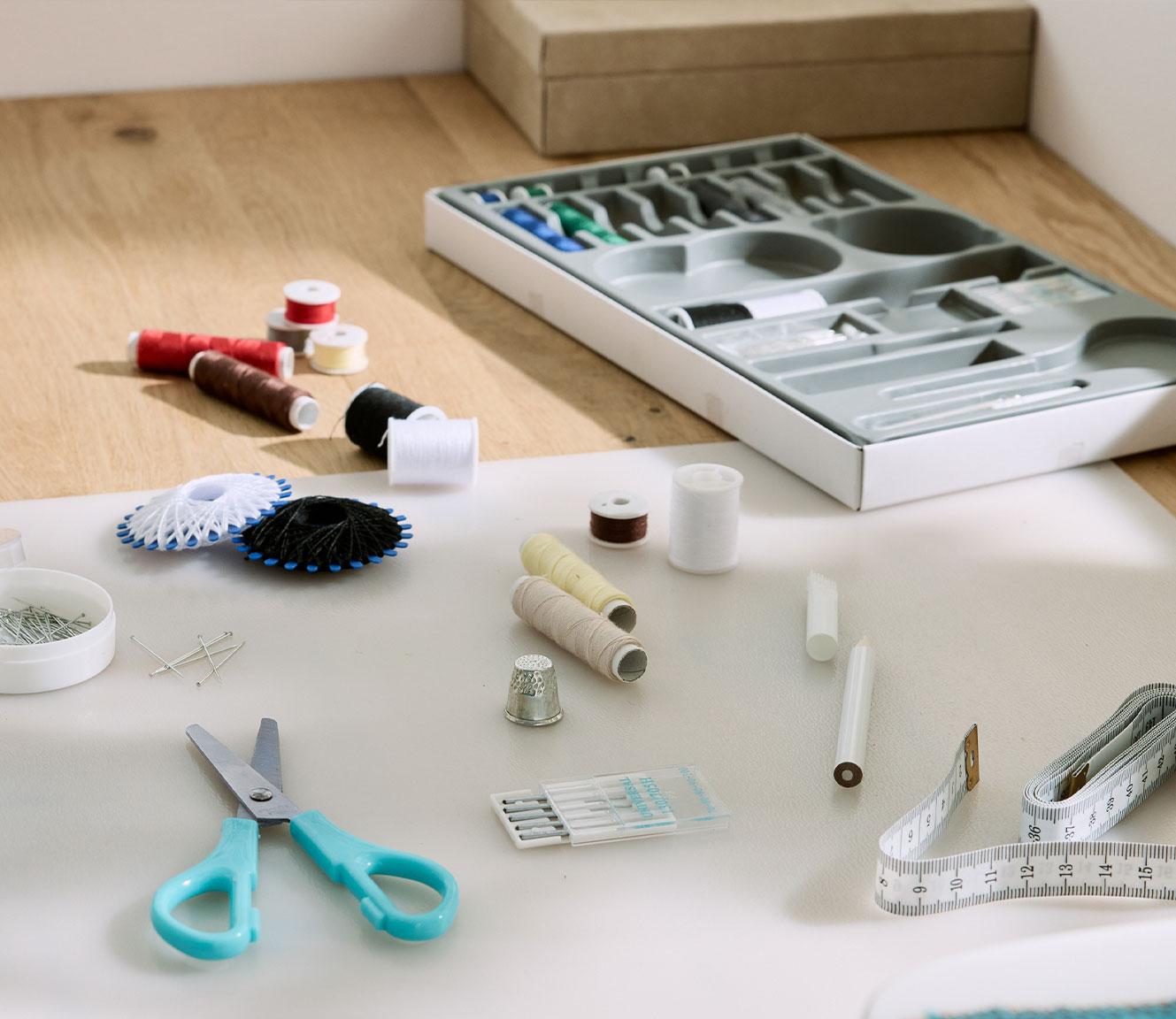 Kit de couture complet avec ciseaux, fils, aiguilles et mètre ruban sur une table.