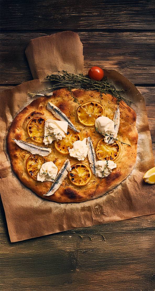 Pizza artisanale garnie d'anchois, de fromage frais et de citron grillé.