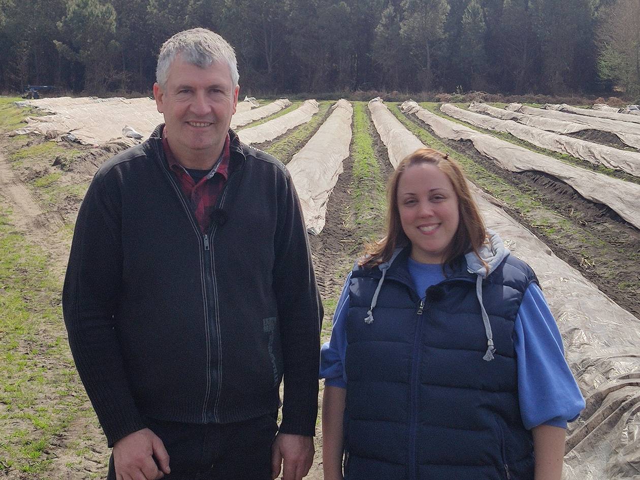 Deux agriculteurs souriants devant un champ d'asperges couvertes de bâches.
