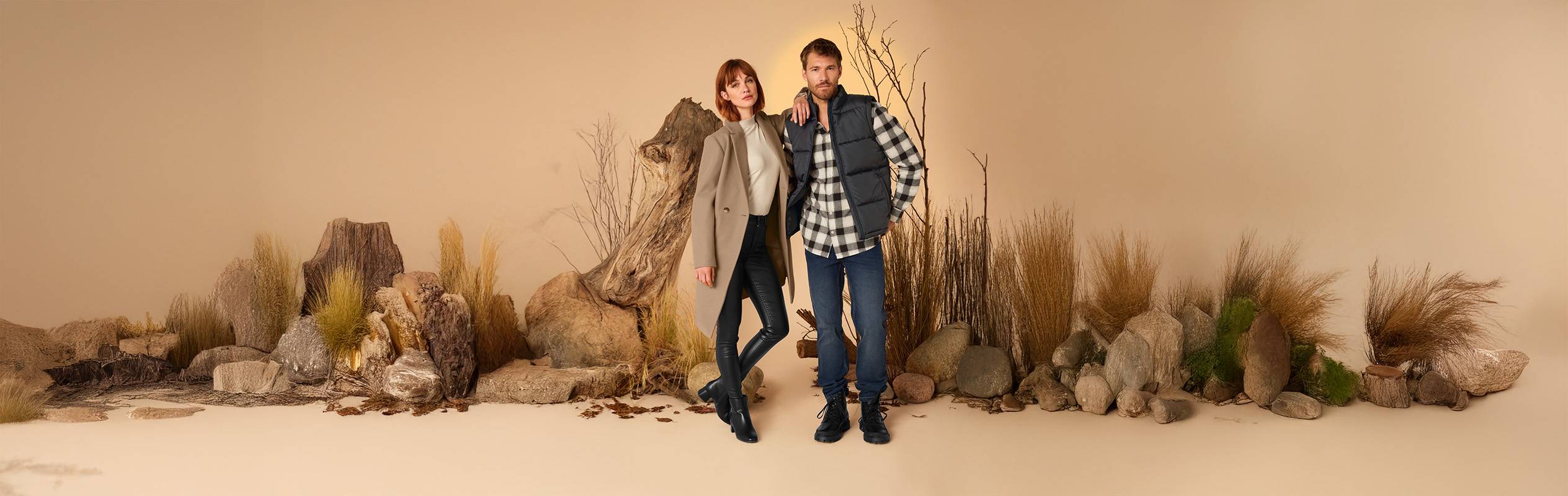 Un homme et une femme posent dans des tenues décontractées d'automne au milieu de rochers et de végétation sèche.