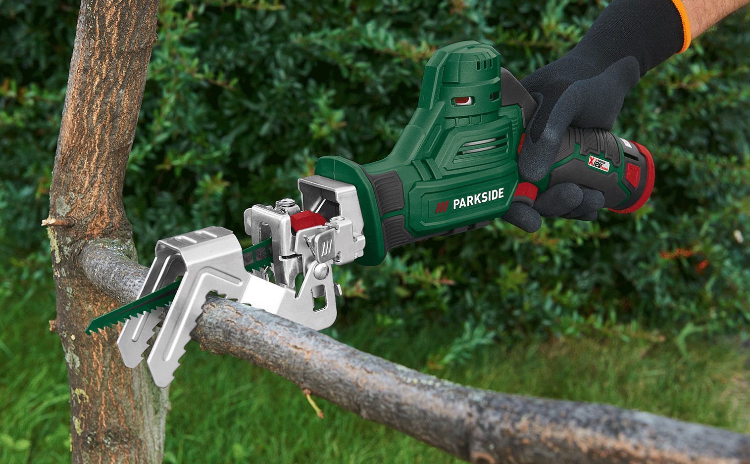 Une scie sabre sans fil verte coupe une branche d'arbre, tenue par une main gantée.
