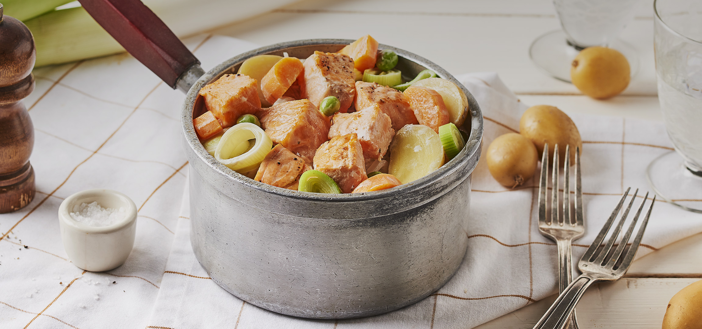 Saumon et légumes cuits dans une casserole, avec un moulin à poivre et des pommes de terre.