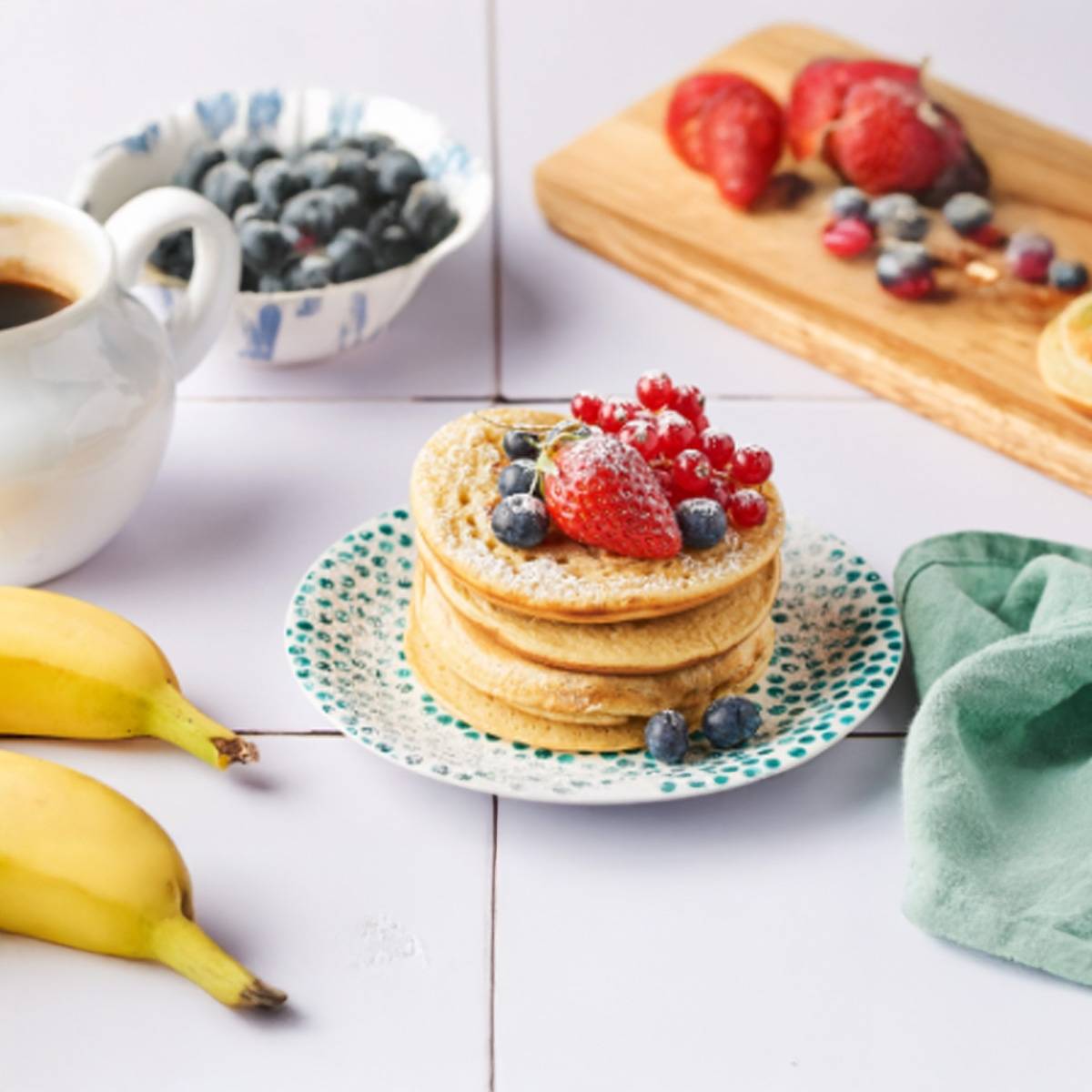 Des pancakes empilés, garnis de fruits rouges et de myrtilles, servis avec des bananes et des baies.