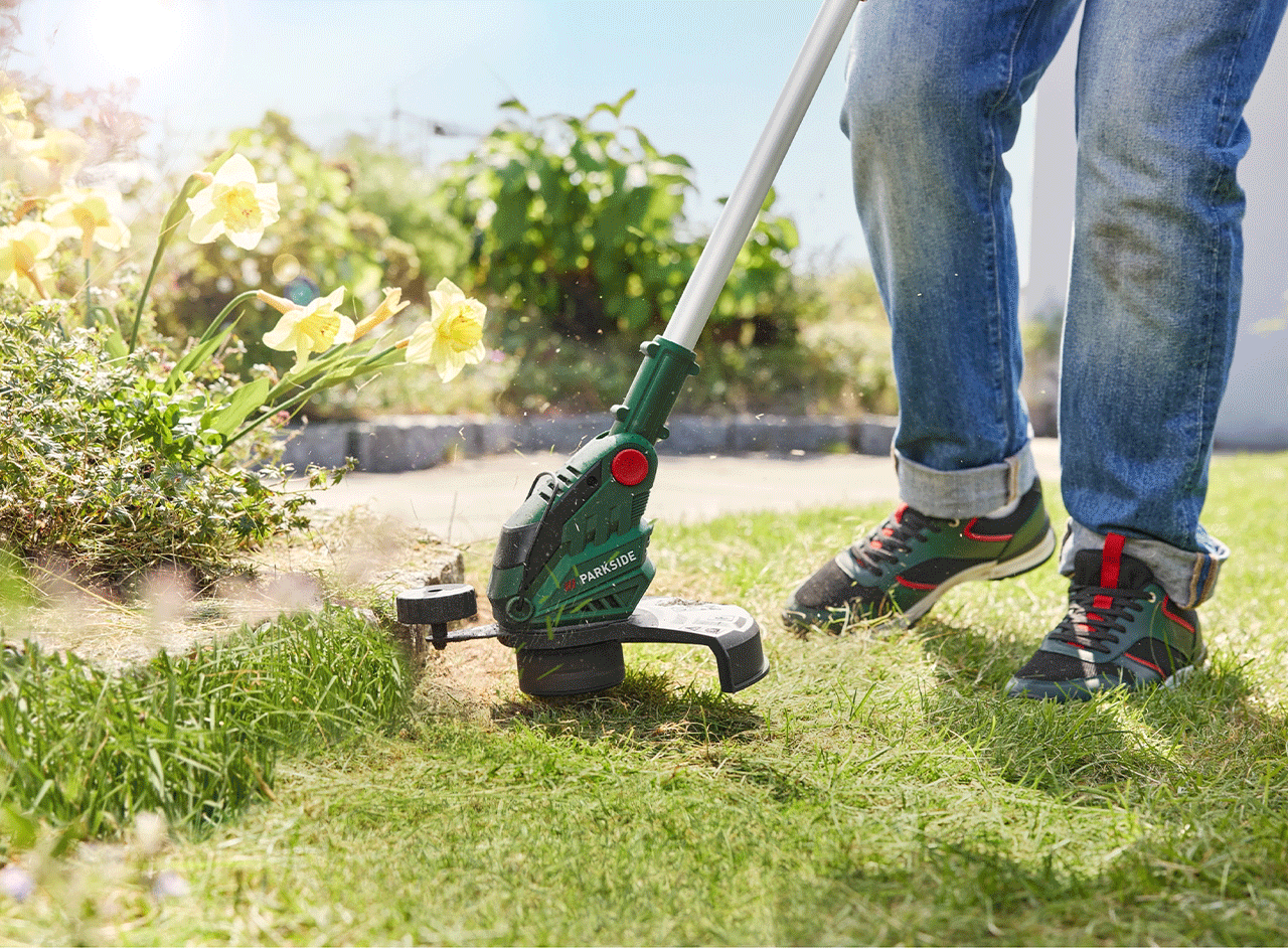 Une personne utilise un coupe-bordure Parkside pour tailler l'herbe le long d'une allée.
