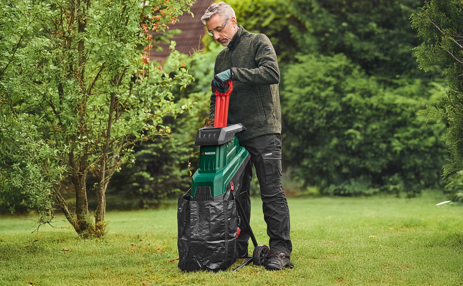 Un homme utilise un broyeur de végétaux dans un jardin verdoyant.