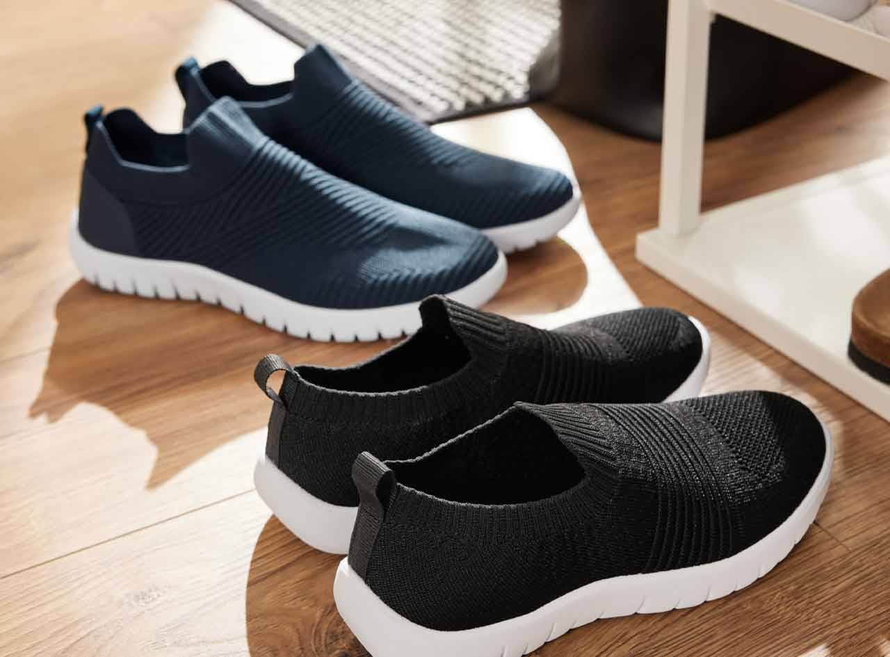 Deux paires de chaussures de sport décontractées, une bleue marine et une noire, reposent sur un sol en bois.