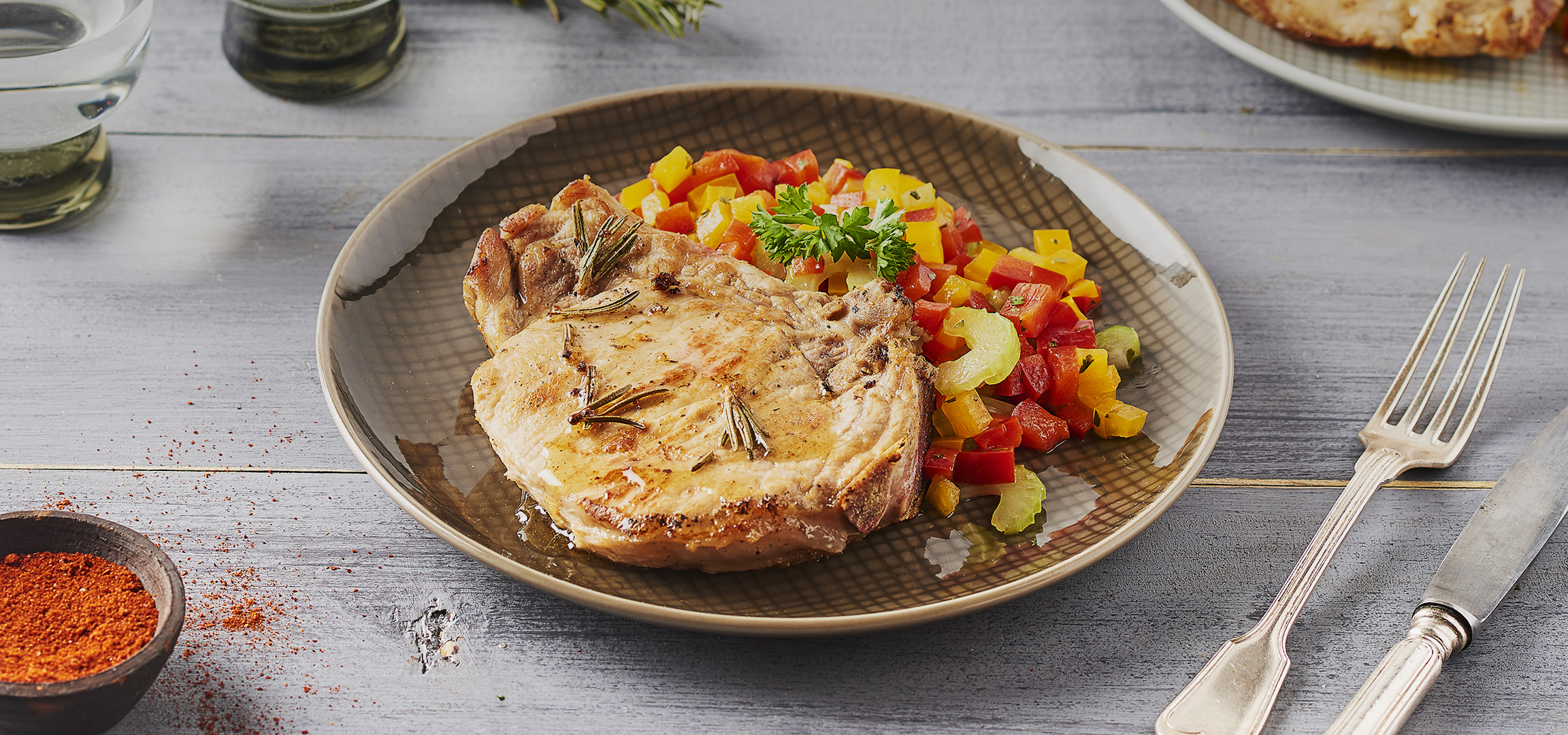 Côtelette de porc grillée avec des poivrons rouges et jaunes coupés en dés sur une assiette.