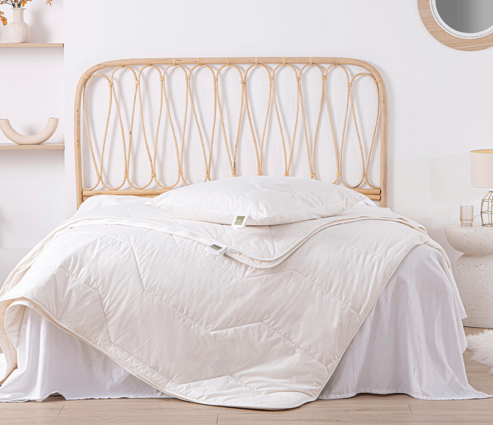 Lit avec tête de lit en rotin, couette et oreiller blancs, table de chevet et miroir.