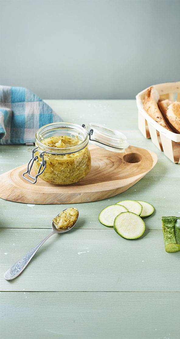 Un pot de confiture de courgettes maison sur une planche en bois, accompagné de tranches de courgettes fraîches.