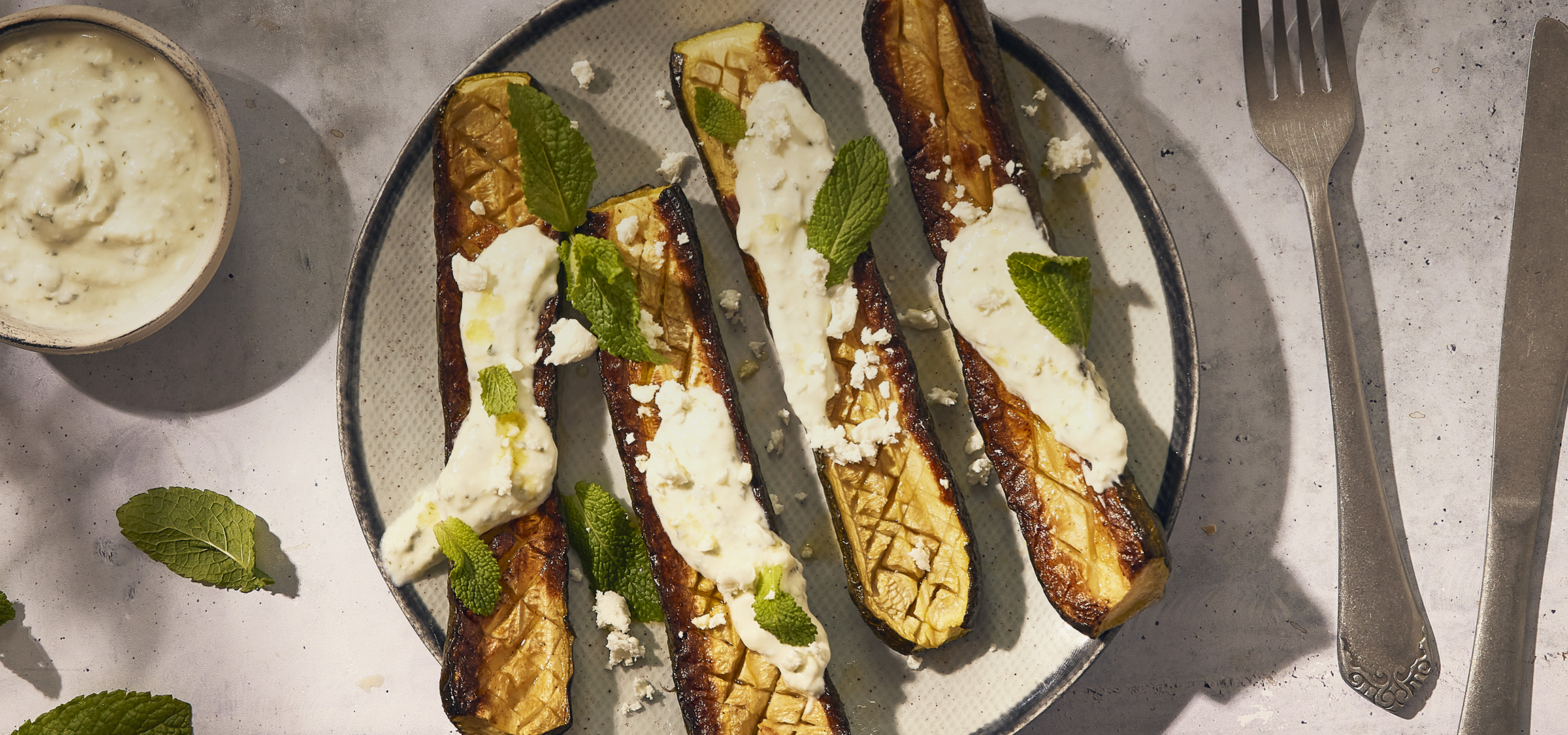 Aubergines grillées avec sauce blanche, fromage émietté et feuilles de menthe.