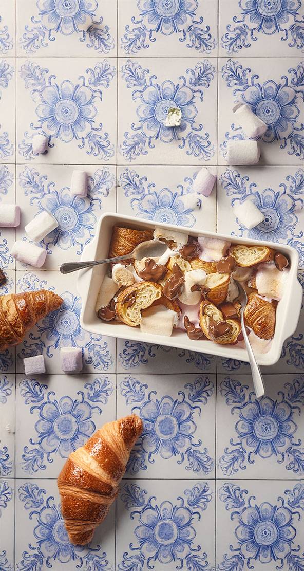 Un plat de croissants, guimauves et chocolat fondu sur un carrelage bleu et blanc.
