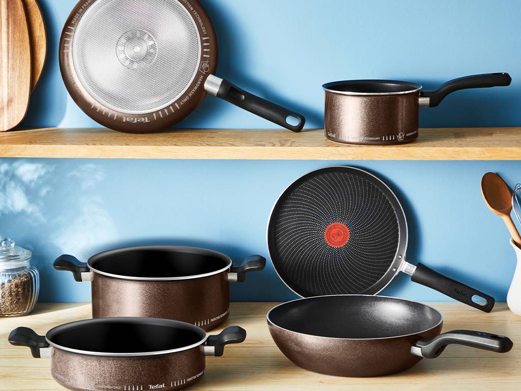 Batterie de cuisine marron et noire sur des étagères en bois, comprenant des casseroles, une poêle et une crêpière.