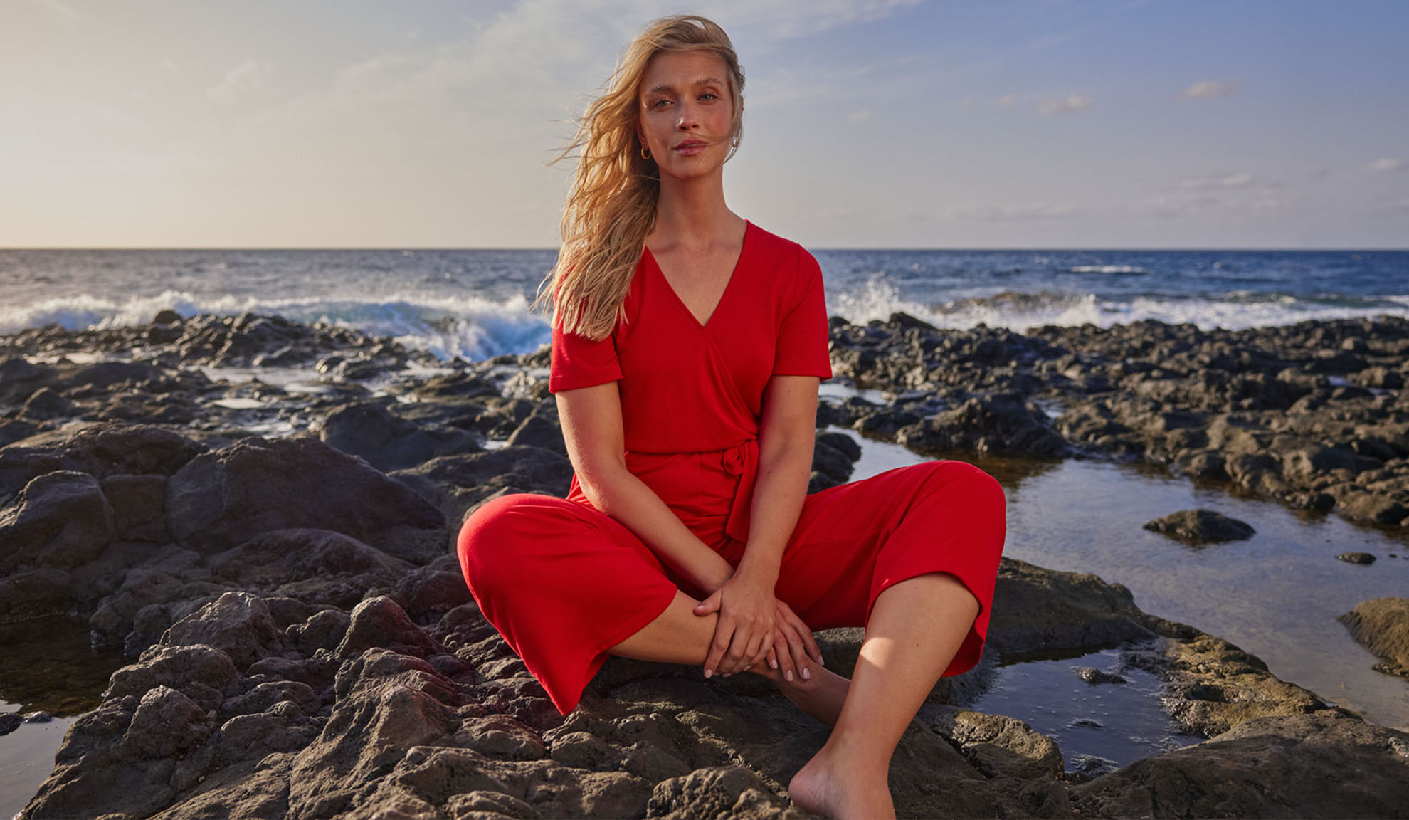Femme en combinaison rouge assise sur des rochers au bord de la mer.