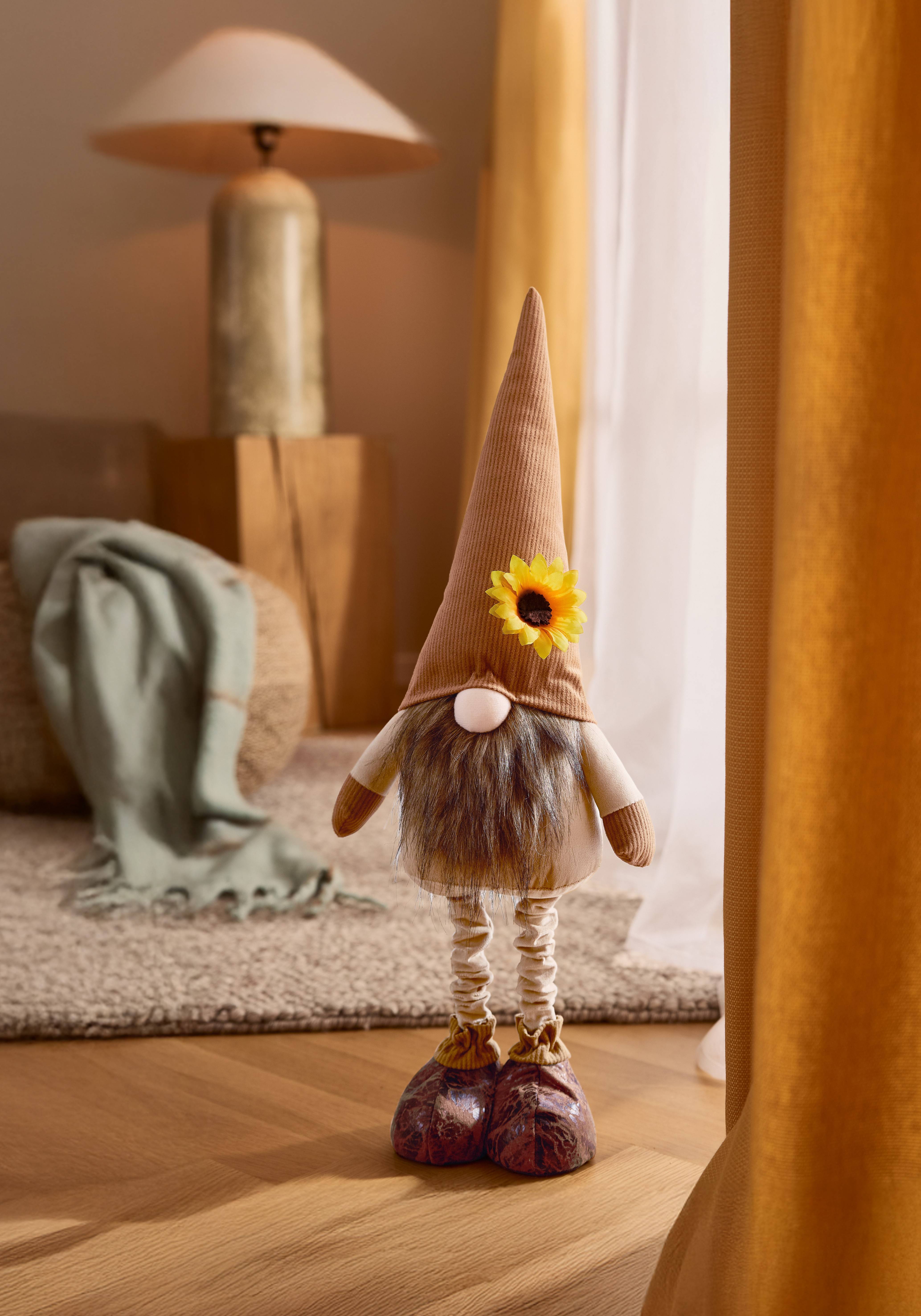 Un gnome en peluche avec un chapeau marron et une fleur de tournesol, posé sur un parquet.