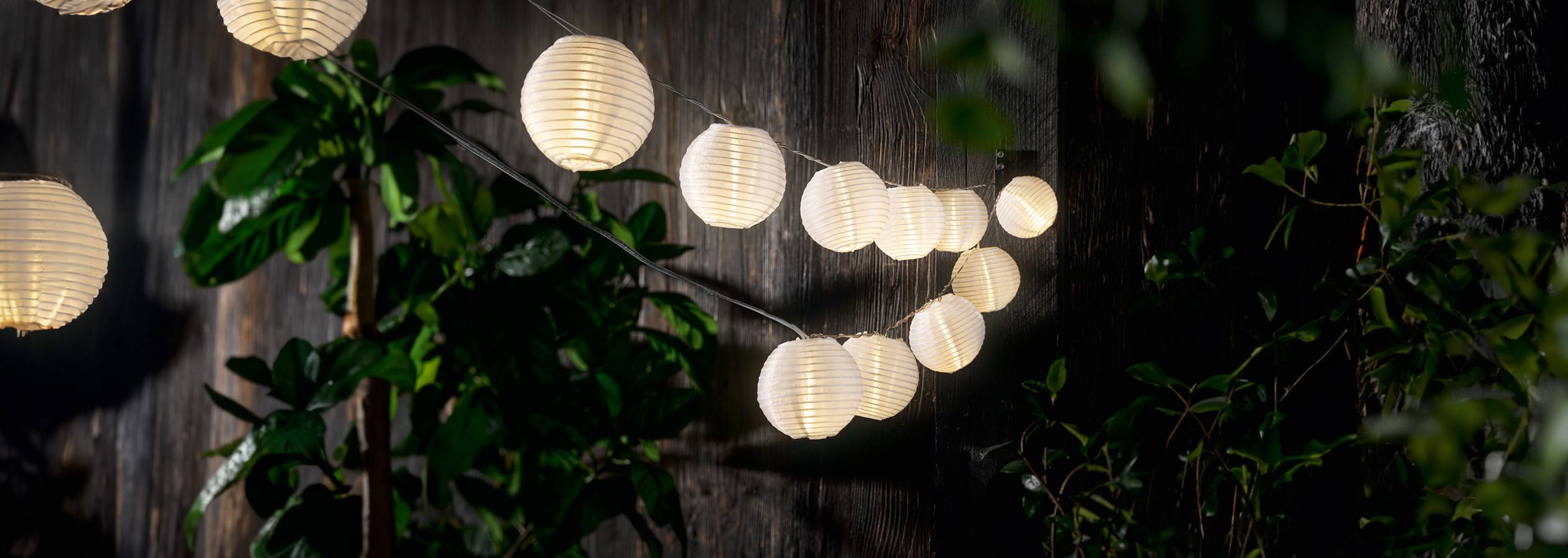 Guirlande lumineuse extérieure avec lanternes en papier blanc accrochées à un mur en bois.
