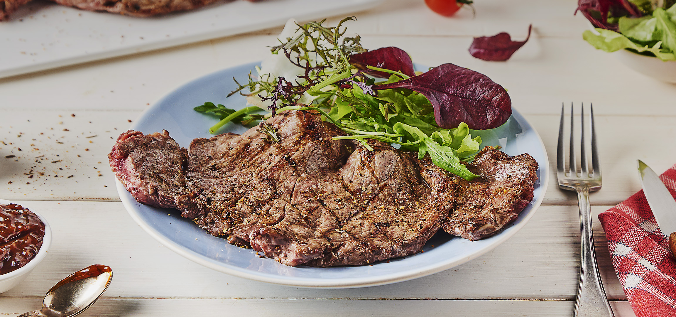 Steak grillé avec salade verte fraîche et sauce barbecue sur une table en bois.