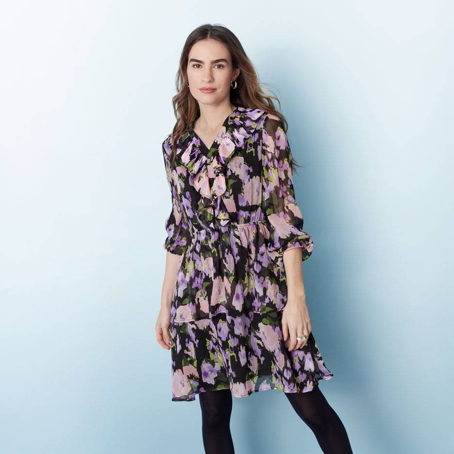 Femme en robe florale noire, violette et rose à volants et collants noirs.