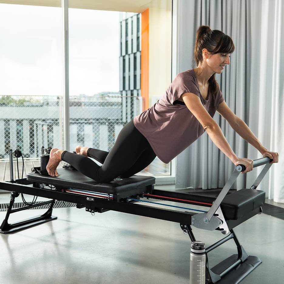 Femme faisant du Pilates sur un reformer avec ressorts et sangles.