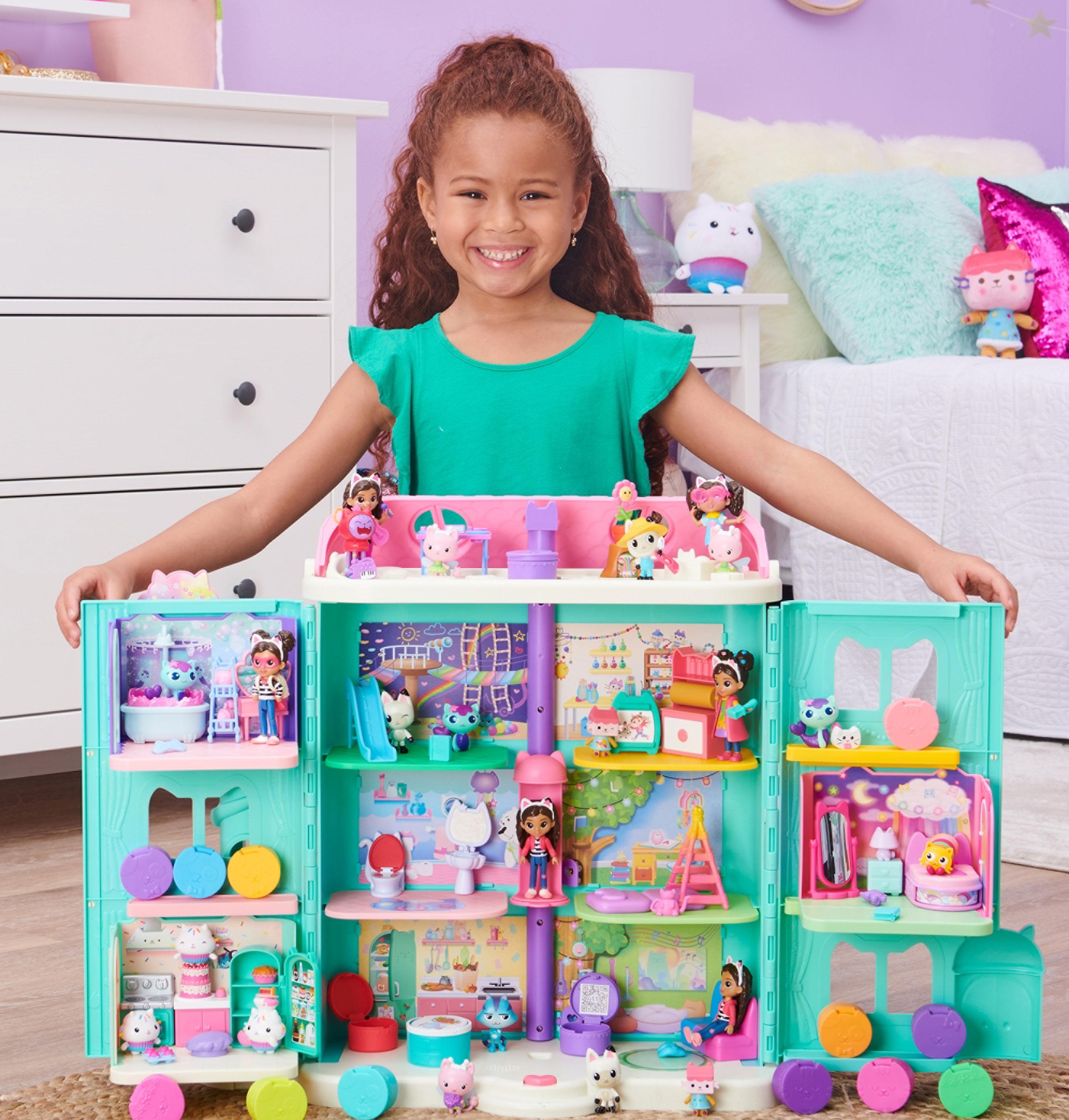 Une petite fille souriante joue avec une grande maison de poupée colorée et ses figurines.