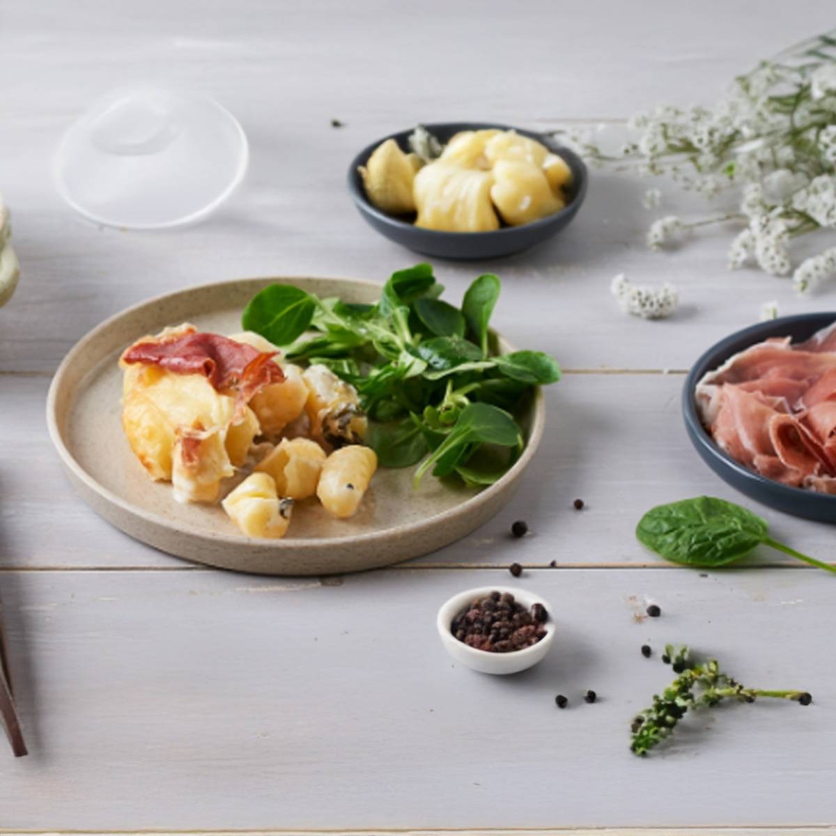 Un plat de gnocchi gratiné au fromage et jambon, servi avec une salade et du poivre.