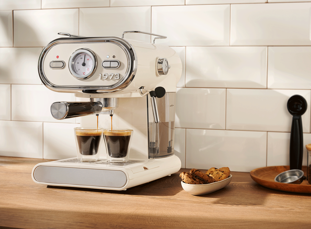 Machine à expresso rétro crème avec deux tasses de café et des biscuits sur un comptoir en bois.