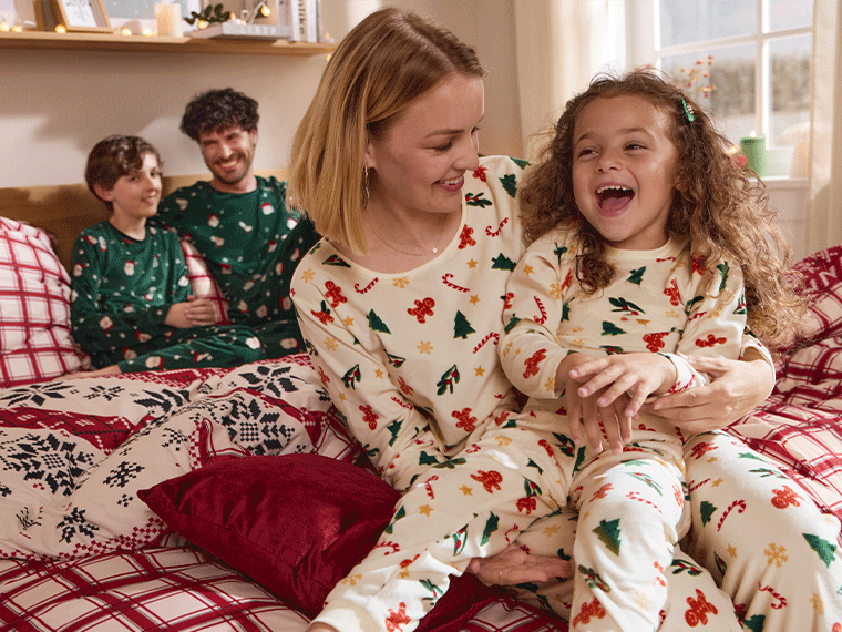 Famille en pyjamas de Noël assortis, riant sur un lit avec une parure de lit à carreaux.