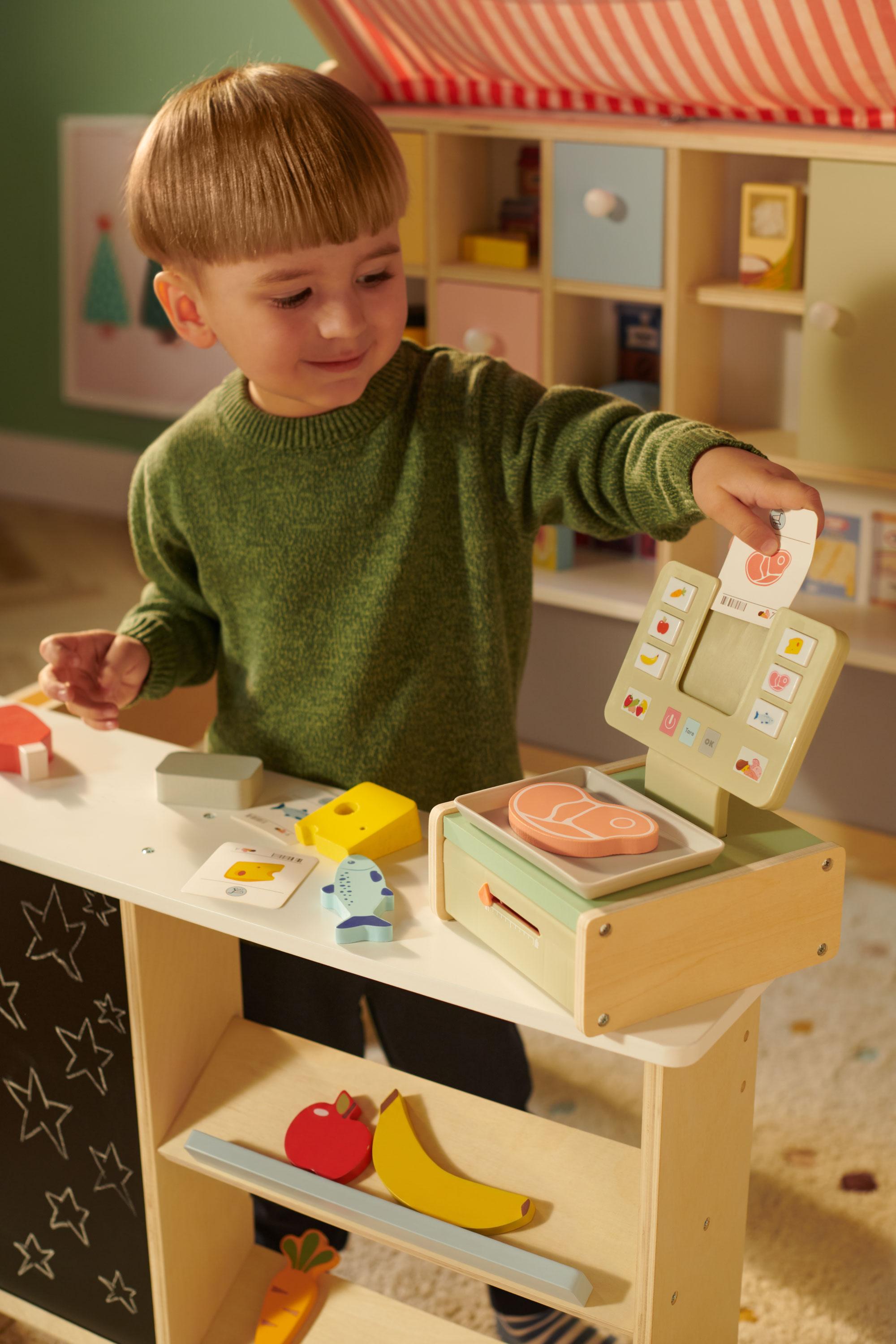 Un jeune garçon s'amuse avec une caisse enregistreuse et une balance en bois pour enfant.