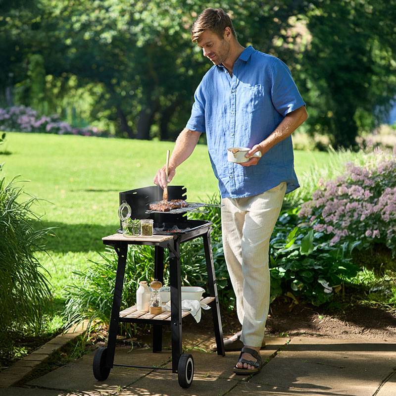Homme grillant des steaks sur un barbecue extérieur.