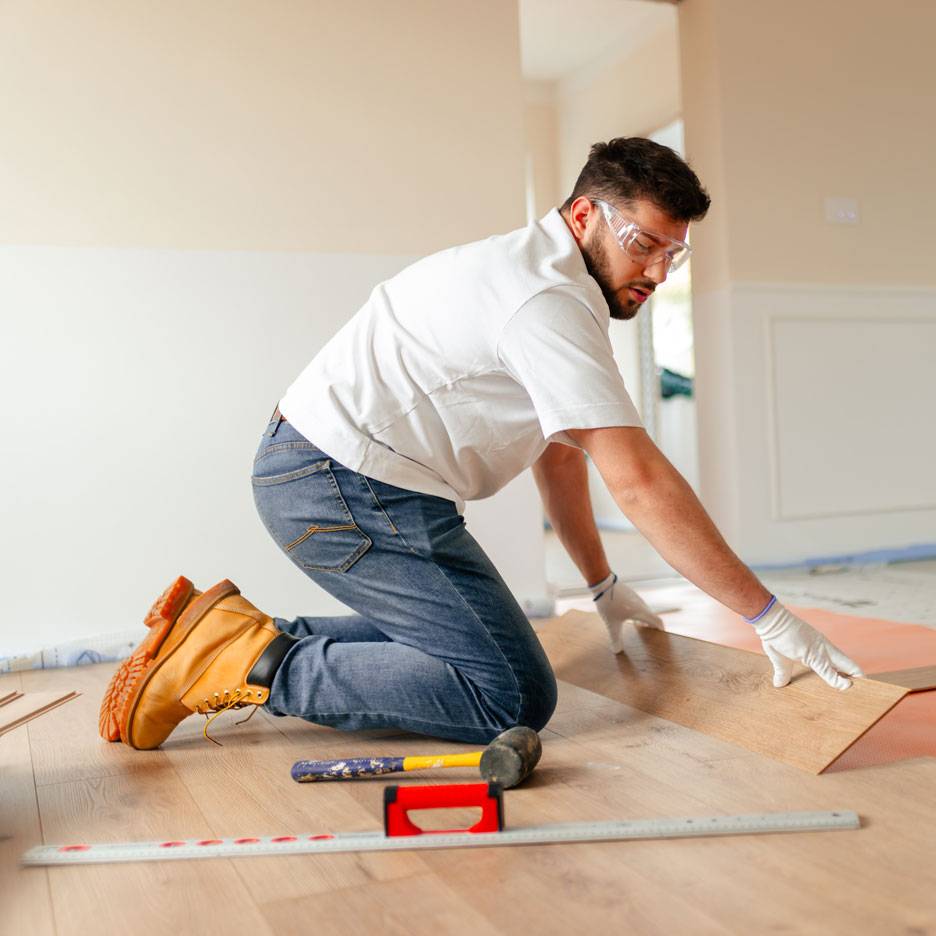 Homme posant du parquet stratifié, portant des lunettes de sécurité et des bottes de travail.