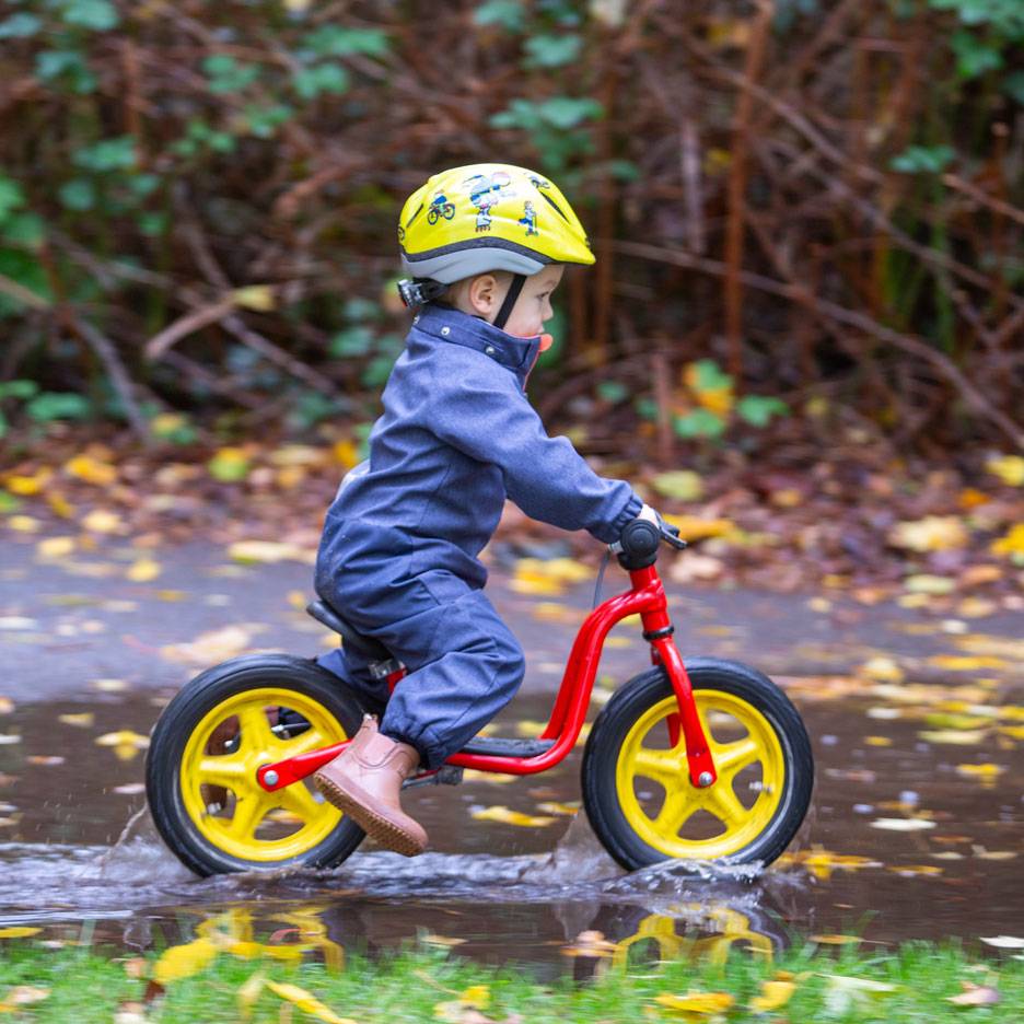 Enfant sur draisienne dans une flaque, avec casque et combinaison.