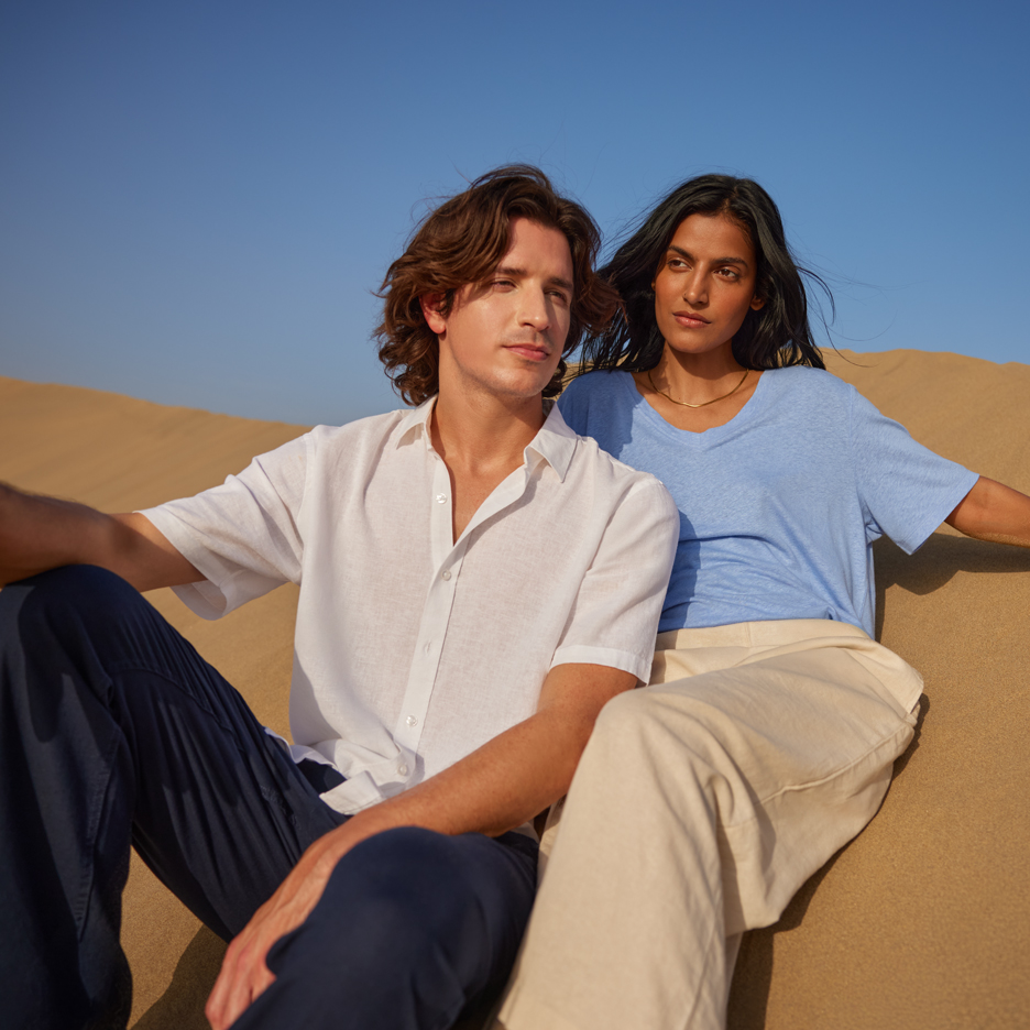 Deux jeunes dans le désert, portant une chemise blanche et un t-shirt bleu, un pantalon bleu marine et beige.