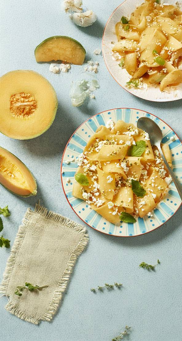 Deux plats de melon cantaloup frais avec du fromage feta et des herbes.