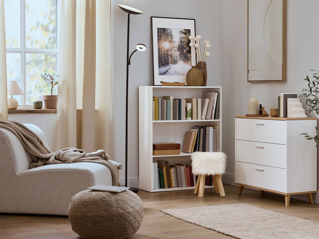 Salon confortable avec fauteuil, bibliothèque et commode aux couleurs neutres.