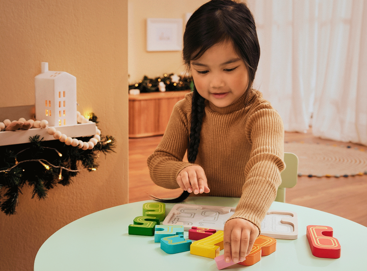 Enfant jouant avec un puzzle de chiffres en bois colorés sur une table verte, décor de Noël.