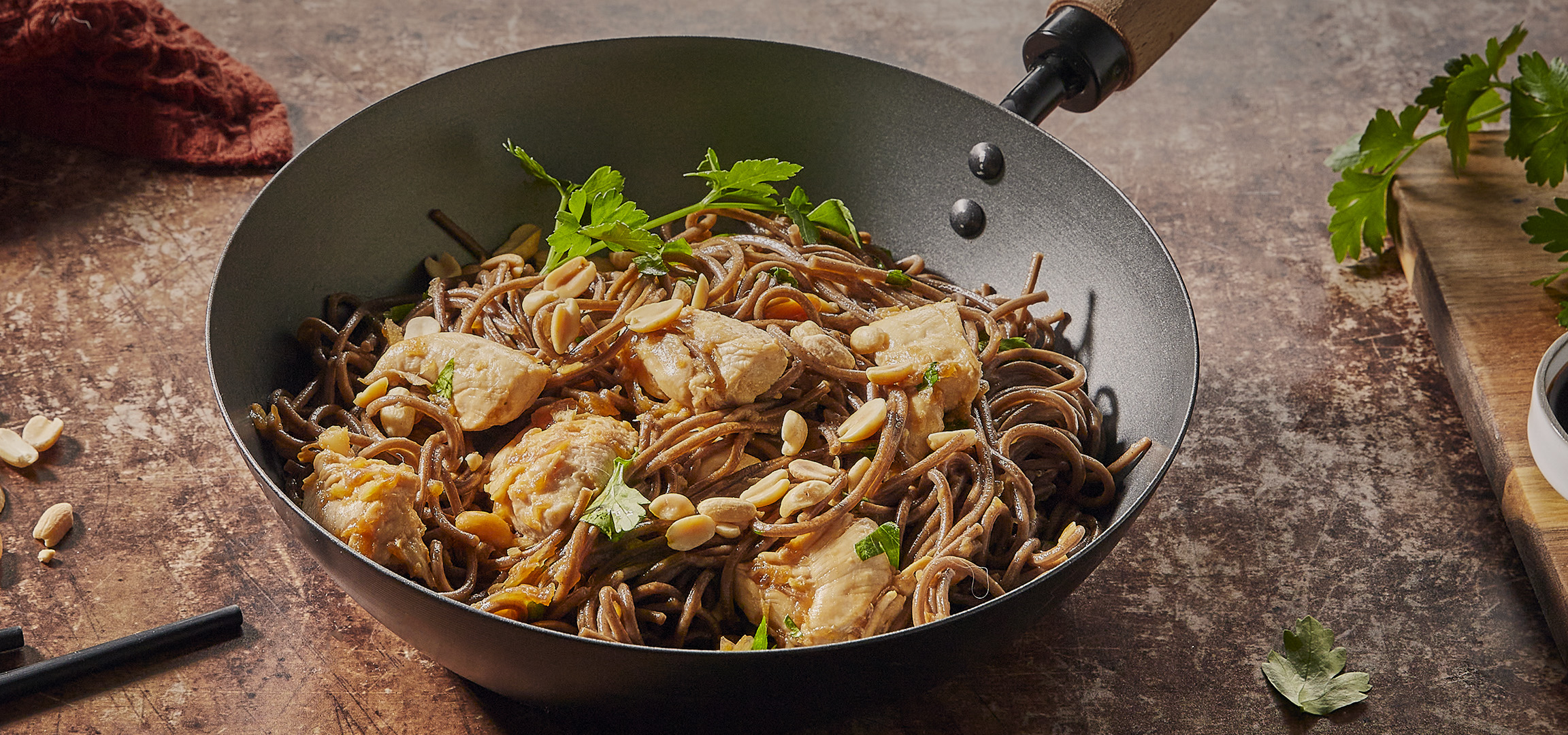 Nouilles soba au poulet et cacahuètes dans un wok, avec de la sauce soja et du persil.