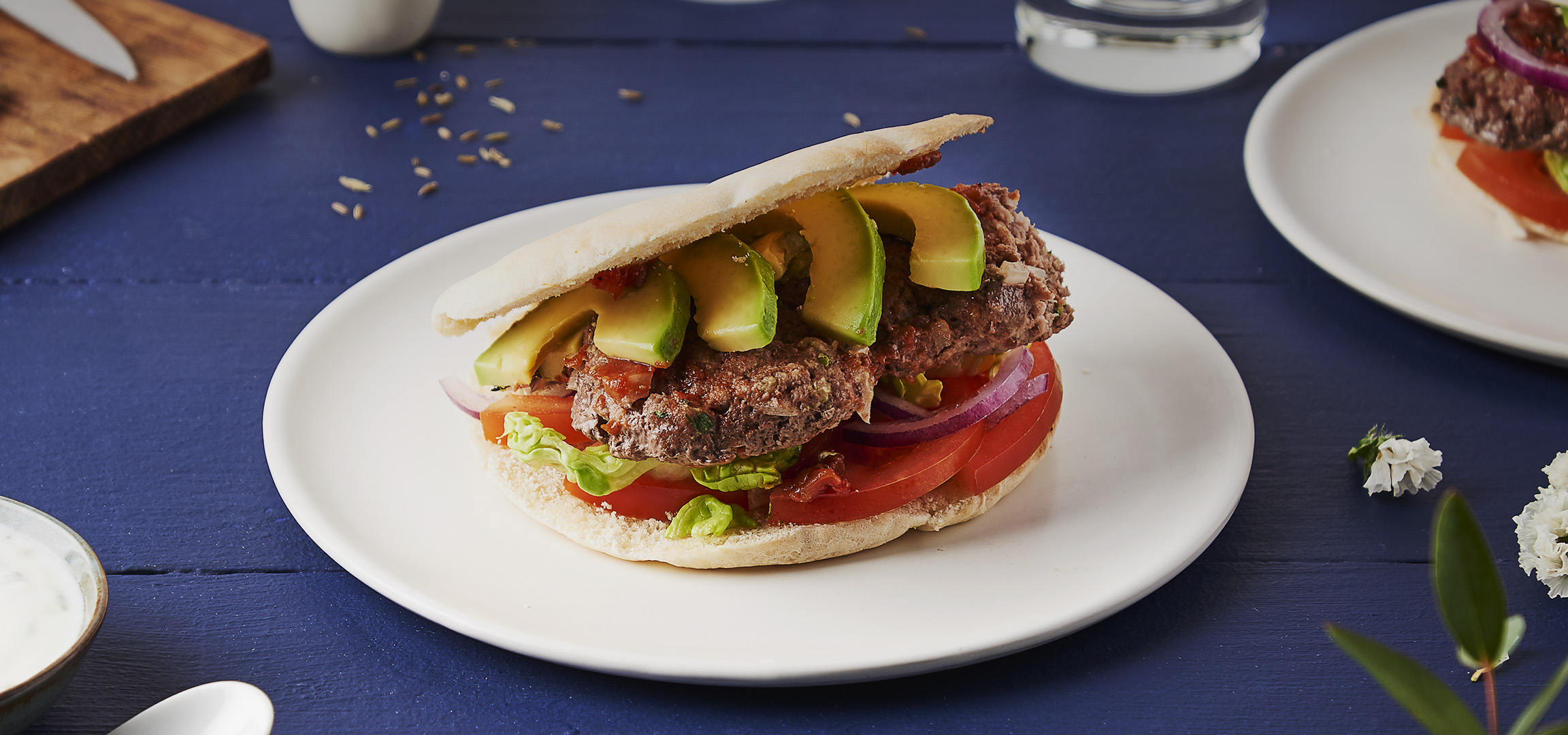 Un burger de bœuf avec avocat, tomate, laitue et oignon rouge dans un pain pita.