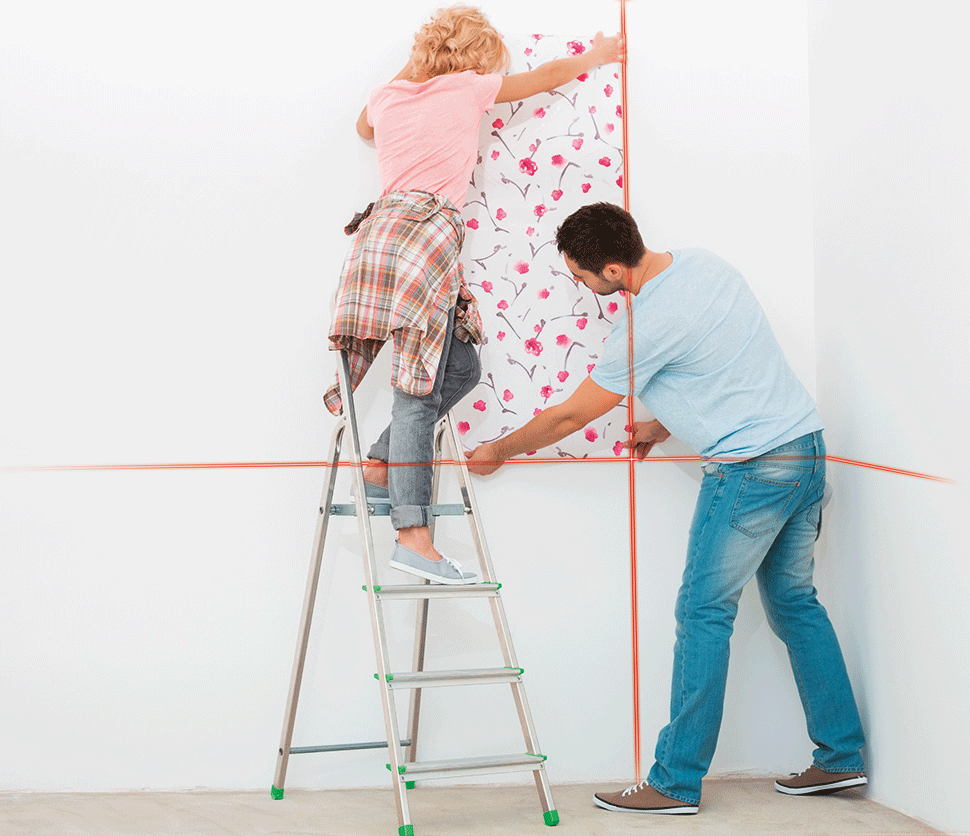 Un couple pose du papier peint à motifs floraux avec un niveau laser.