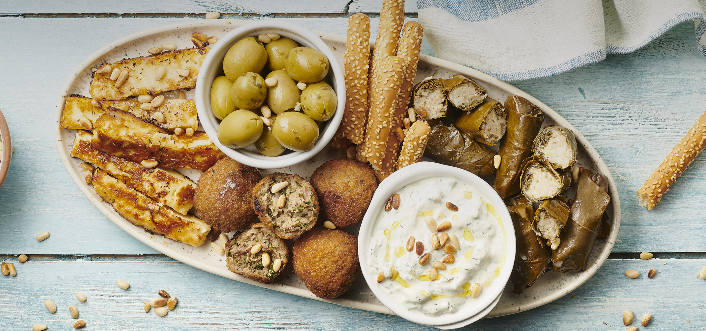 Assortiment de mezzés avec halloumi grillé, olives, kibbeh, dolmas, tzatziki et gressins.