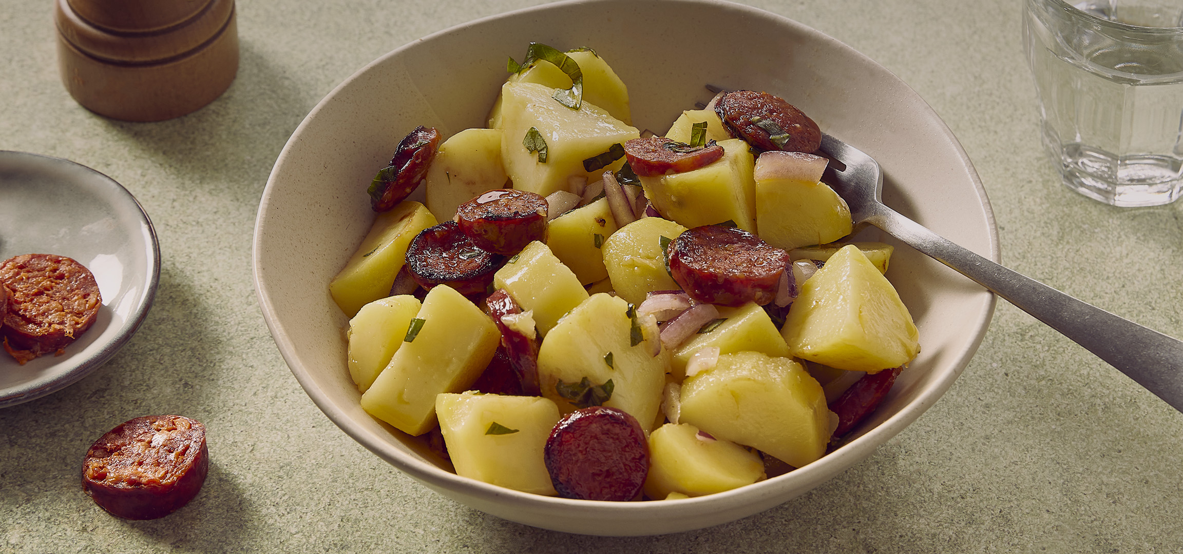 Salade de pommes de terre et de chorizo dans un bol, avec des tranches de chorizo sur une assiette.