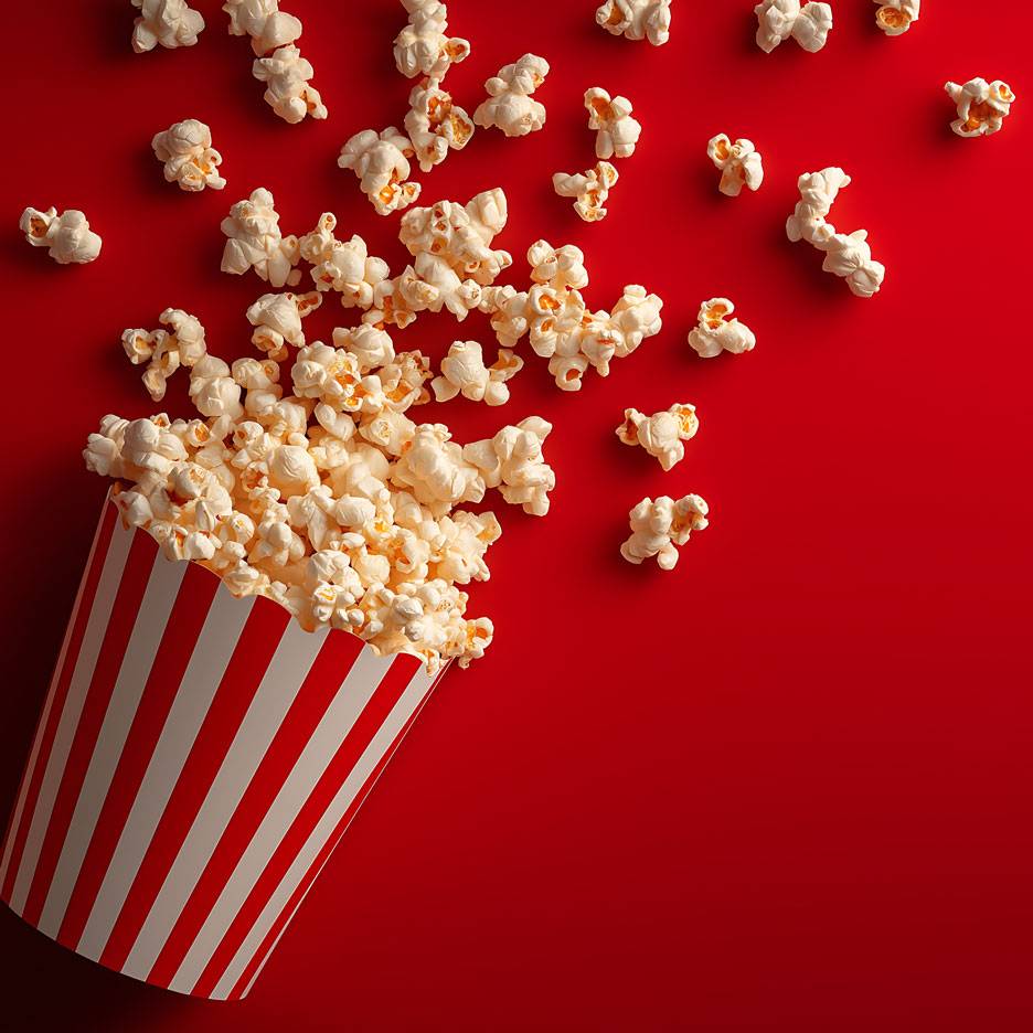 Popcorn sur fond rouge, une partie du popcorn dans un gobelet en carton rayé.