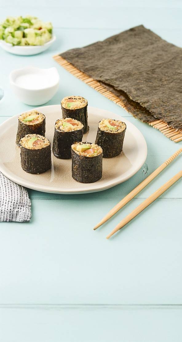 Six maki au quinoa, avocat et saumon, présentés sur une assiette avec des baguettes.