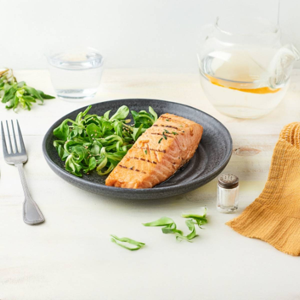 Un saumon grillé servi avec une salade verte sur une assiette noire.