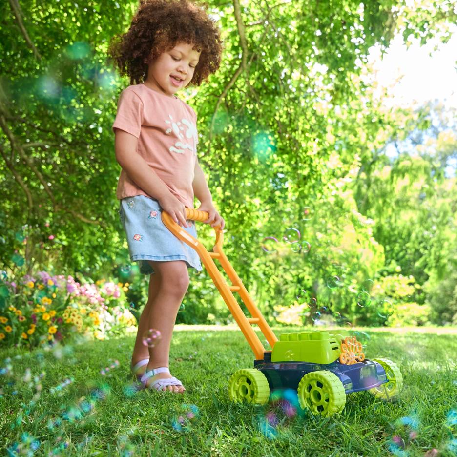 Un enfant aux cheveux bouclés pousse une tondeuse à gazon à bulles sur l'herbe verte.