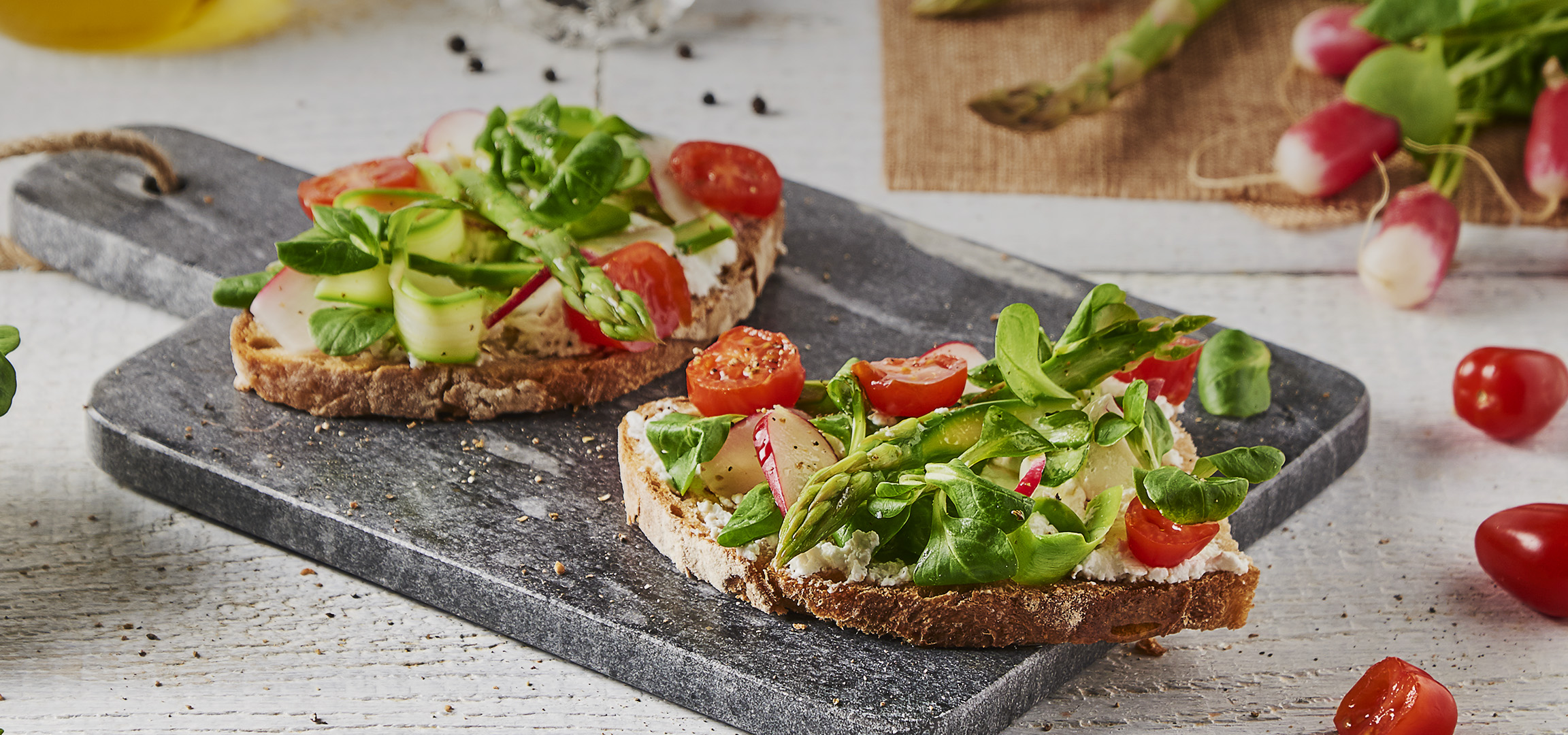 Bruschetta fraîche avec asperges, tomates cerises, radis et salade sur une planche en ardoise.