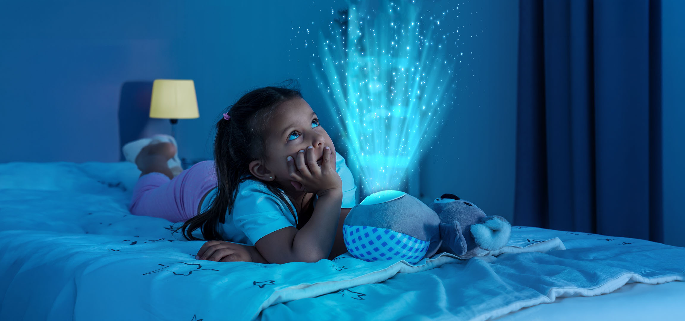 Fille allongée dans son lit, regardant un projecteur d'étoiles illuminant le mur.