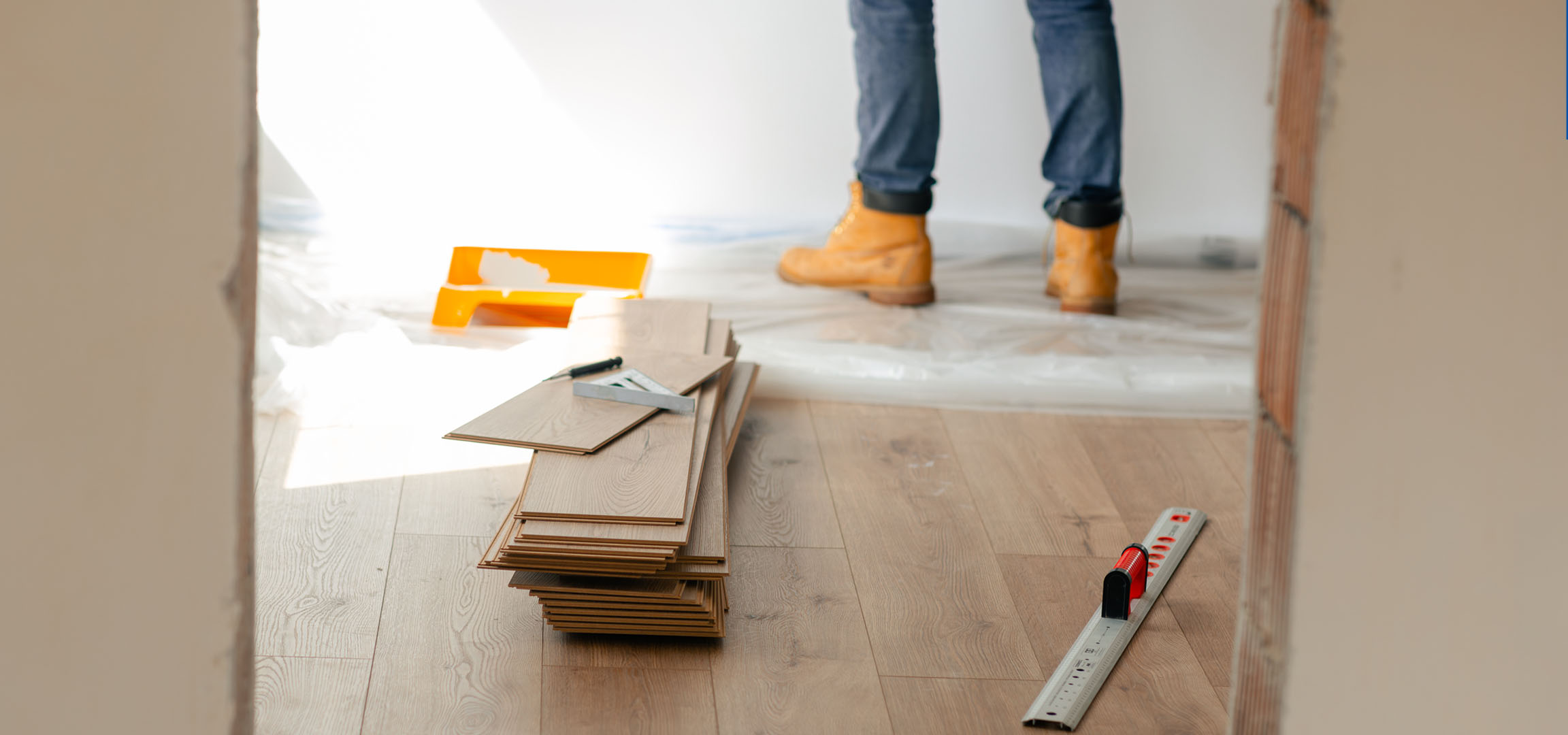Planches de parquet stratifié et outils de pose sur un sol en bois, avec une personne en bottes.