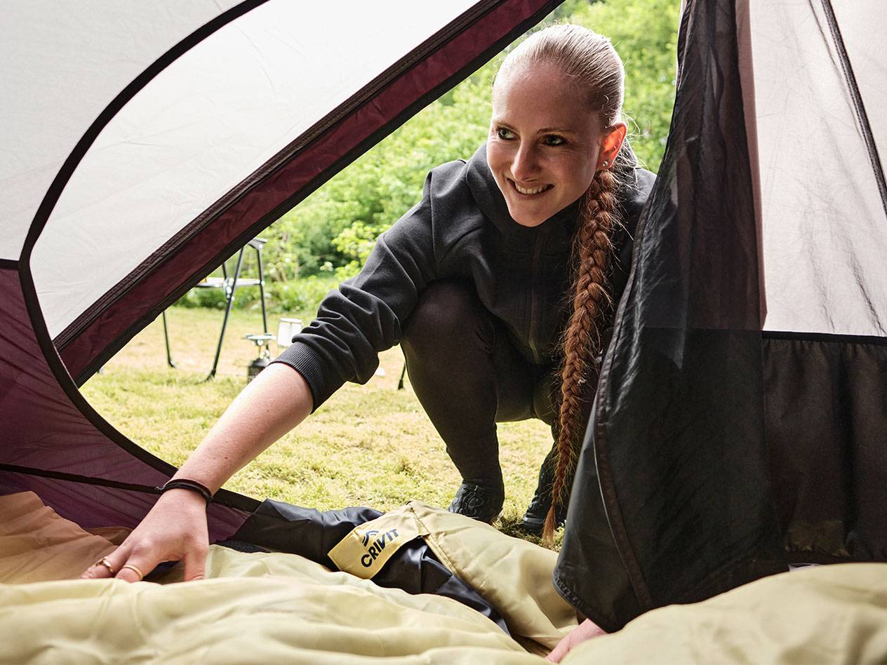 Une femme range un sac de couchage Crivit dans une tente.