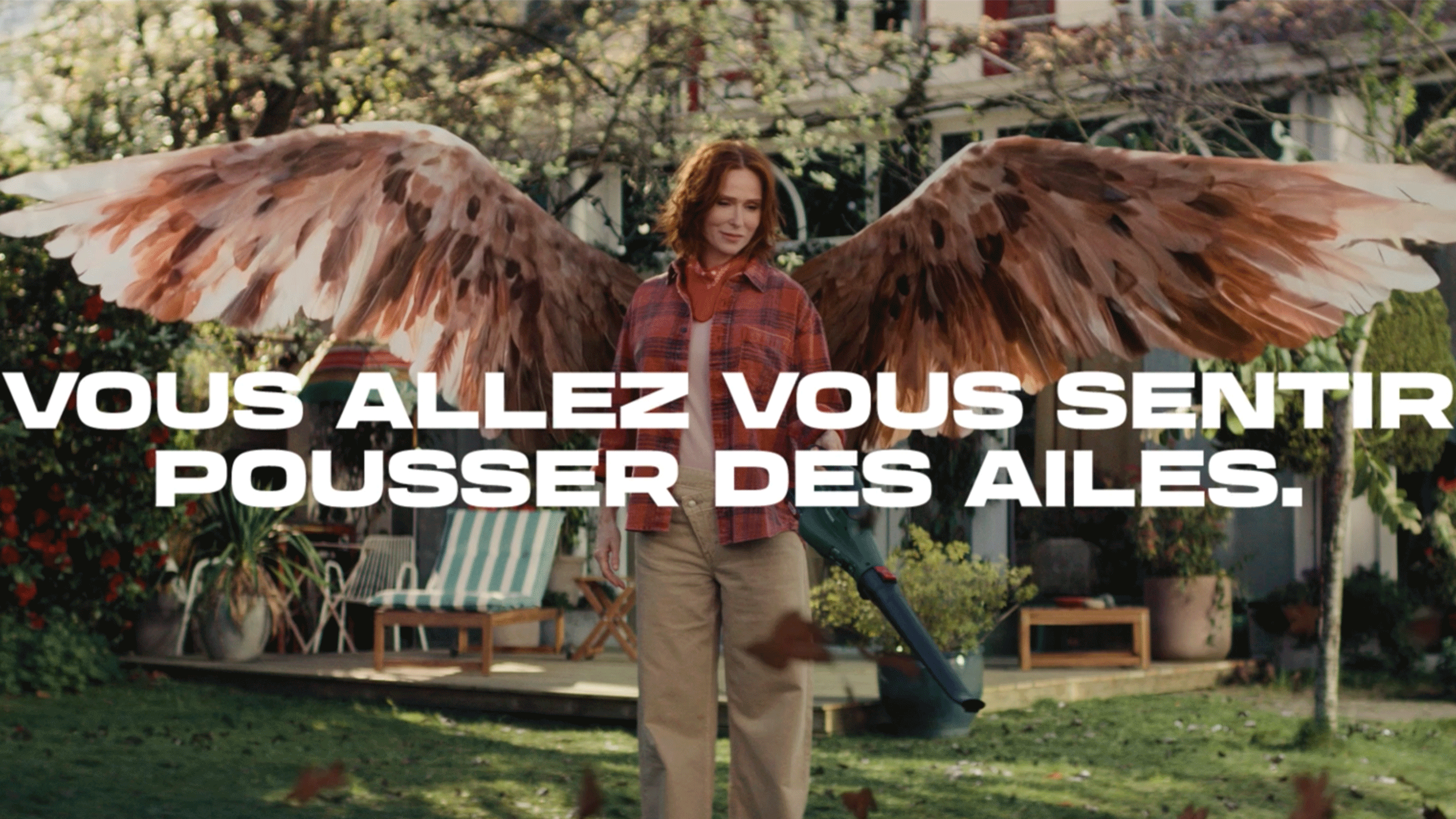 Une femme avec des ailes de plumes tient un souffleur de feuilles dans un jardin.