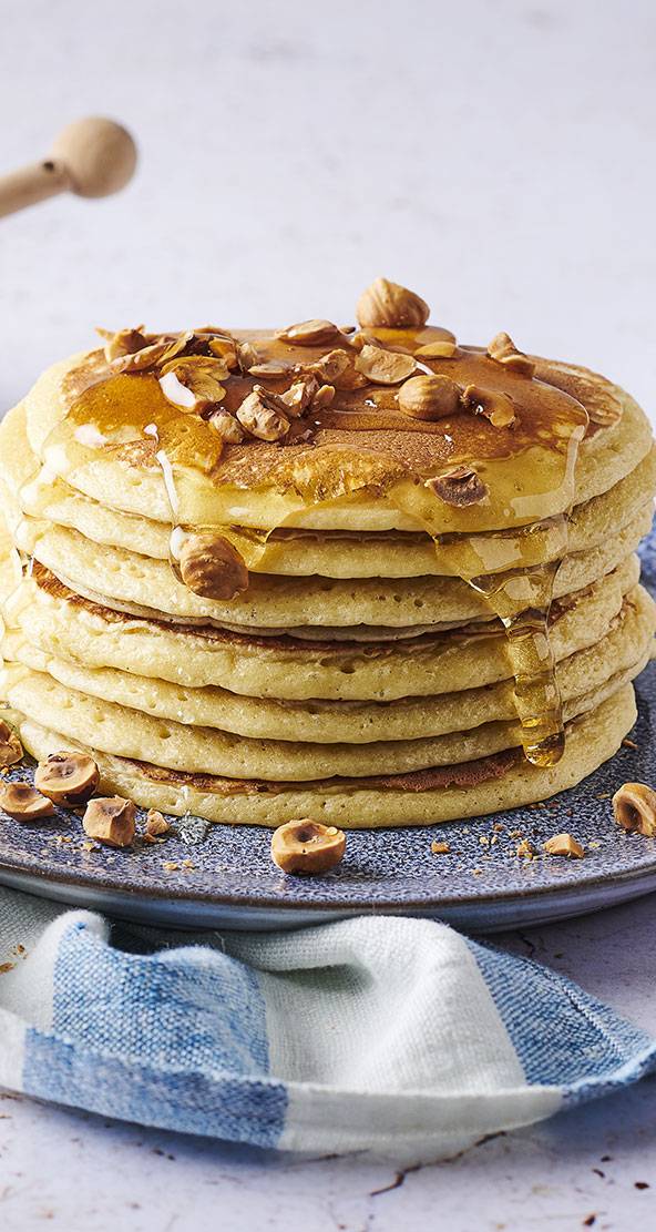 Une pile de crêpes dorées nappées de miel et de noisettes.